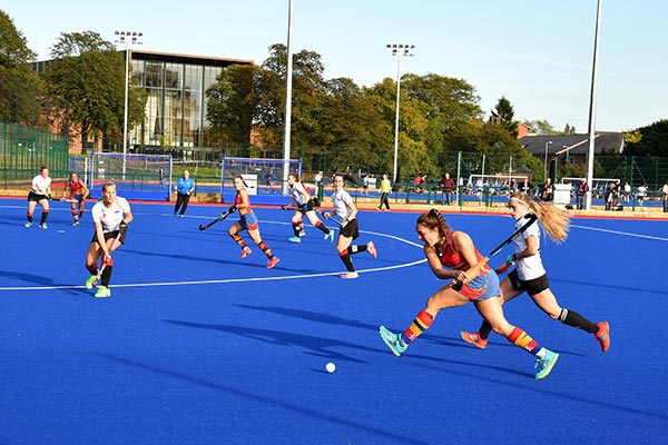 Women playing hockey with a view of the Sport & Fitness club in the background