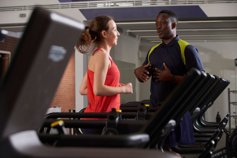 Female running on a treadmill receiving advice from a male gym instructor