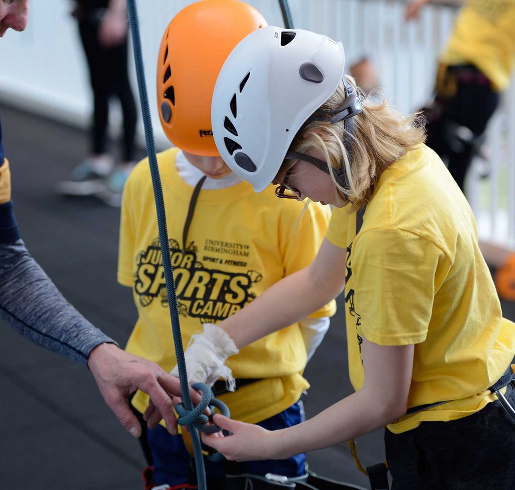Two juniors tying a harness rope for the climbing wall