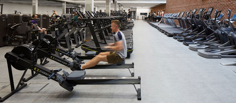 male on the rowing machines with rows of cardio equipment down each side of the gym