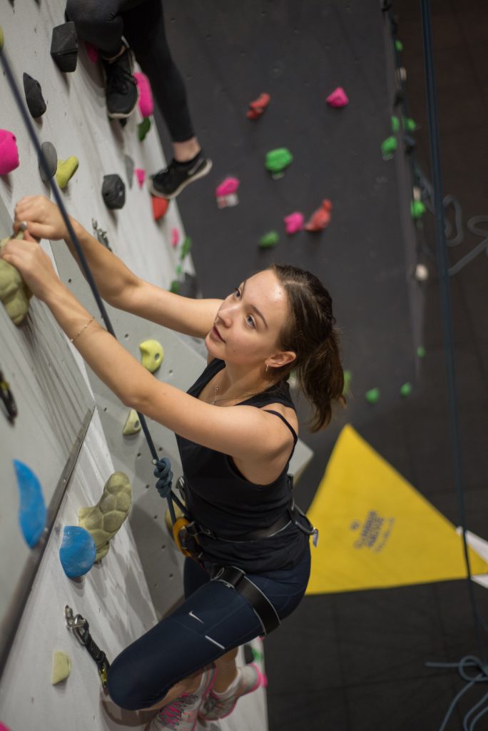 woman climbing with a harness whilst smiling towards the camera