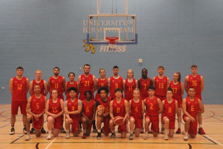 Basketball players from the University of Birmingham pose in front of the basketball hoop in their red match kit