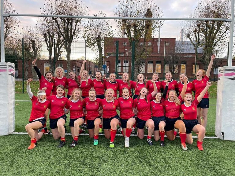 The women's rugby team pose for a celebratory team photo between the rugby posts at University of Birmingham