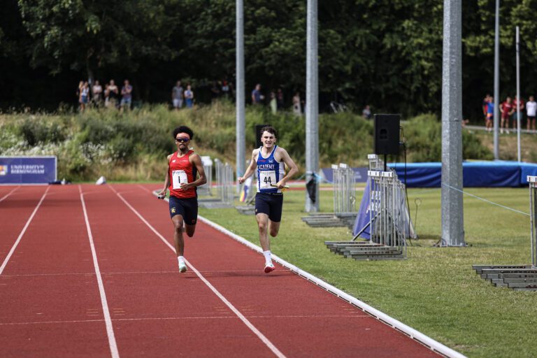 2 men running towards finish line- one from UOB