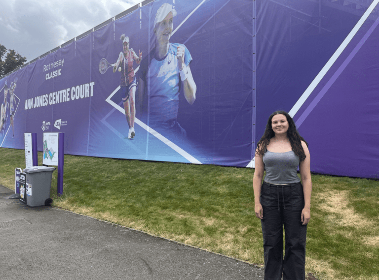 Georgia standing on the right hand side of large banner promoting Rothesay Classic Tennis event