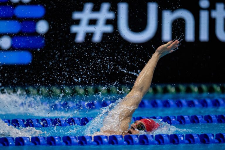 Scholar Ollie Morgan performing the backstroke, arm out of the water wearing a red hat.