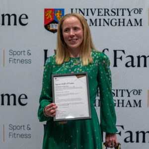 Lora Fachie with her Hall of Fame Award, standing in front of the Sport of Fitness/Hall of Fame sign.