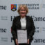 Penny Briscoe holding her Sport Hall of Fame award in front of the University of Birmingham Sport & Fitness backdrop.