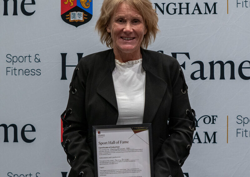 Penny Briscoe holding her Sport Hall of Fame award in front of the University of Birmingham Sport & Fitness backdrop.