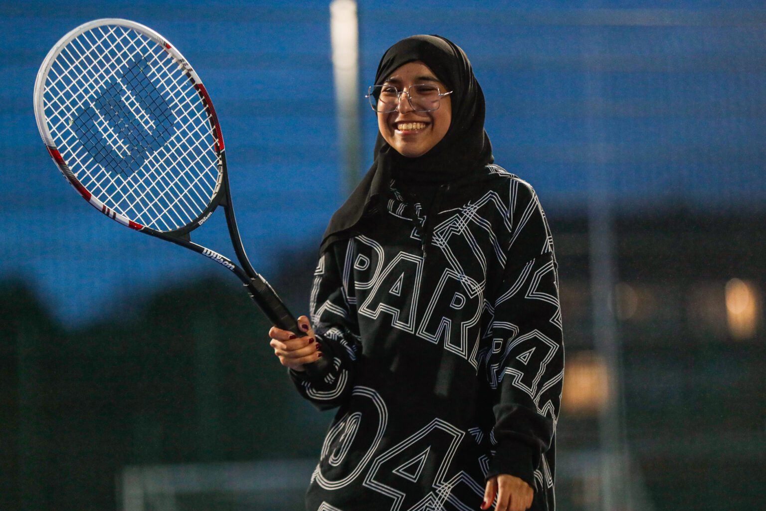 A member of active residences, smiling and holding their tennis racquet in the air.