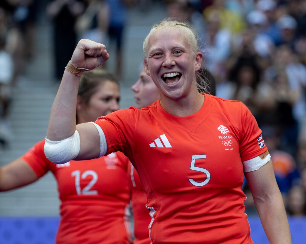 Heather Cowell faces camera in her red Team GB rugby sevens kit, smiling and right fist in the air