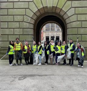 Group of staff and students in high-vis jackets standing in front of the archway of Old Joe, holding litter-picking grabbers