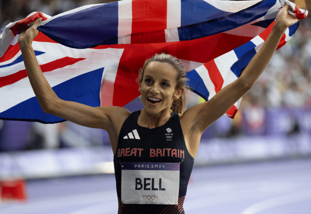 Georgia Bell holds GB flag above her head. She has her GB kit on and her race number.