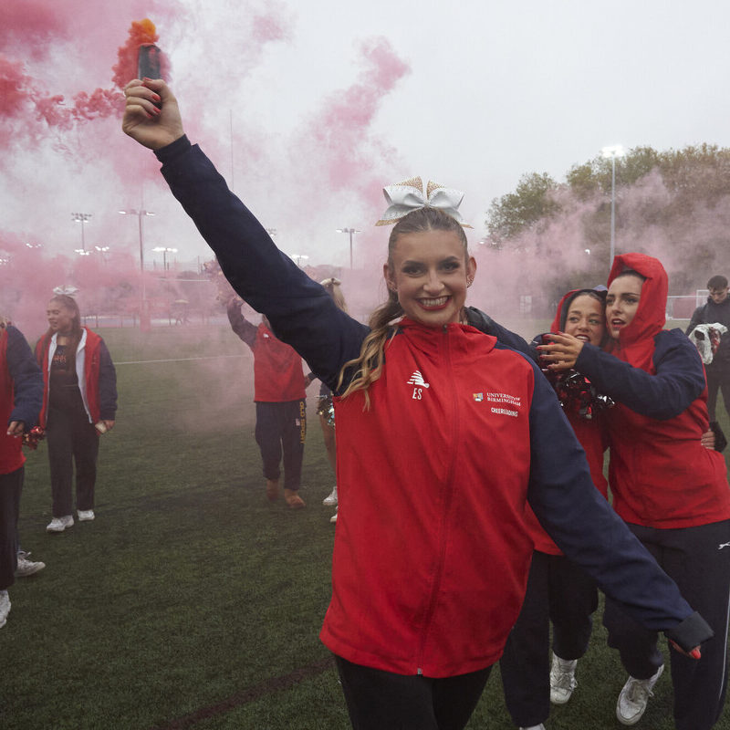 Cheerleader dressed in red UoB kit. Red smoke in the air.