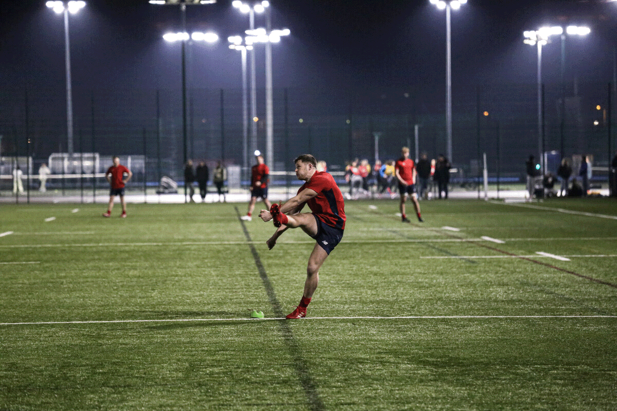 Student kicking a rugby. ball with leg kicked high in the air.