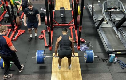 Male deadlifting with other competitors spectating