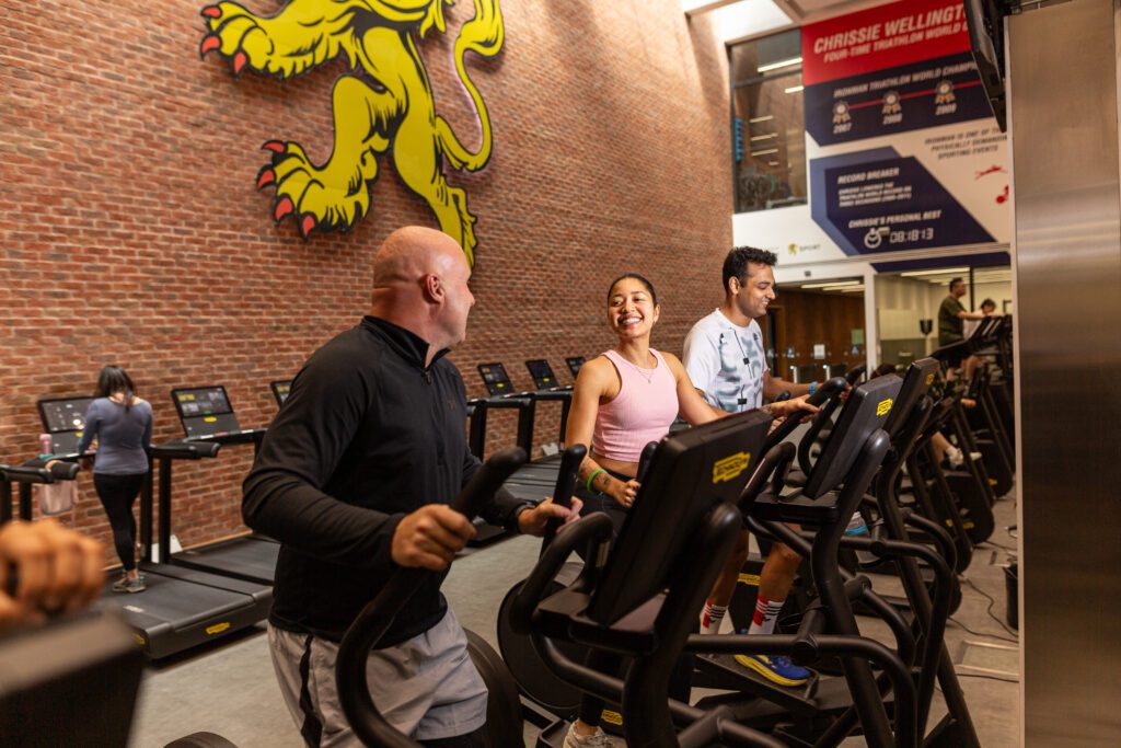 Two men and a woman on cross trainer, smilin at each other