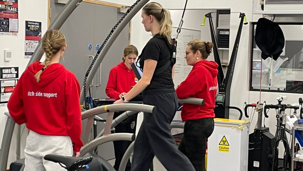 Woman on treadmill in performance lab with concussion student staff supporting