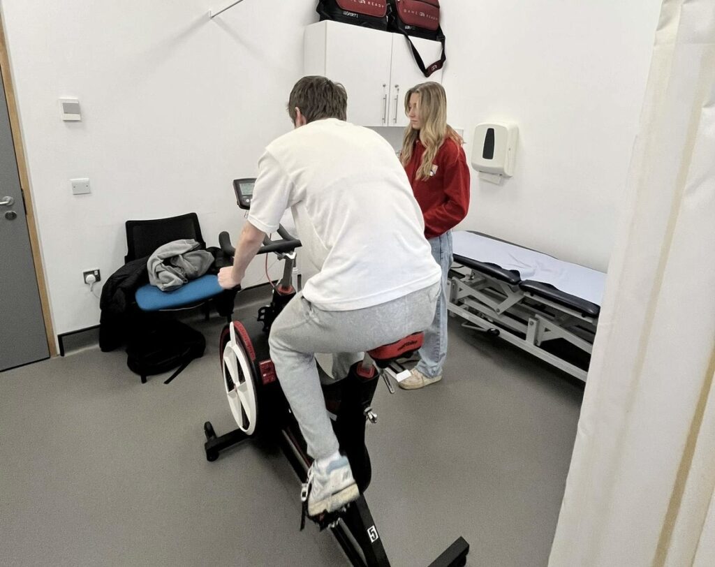 Man on bike in Performance Lab doing testing with support of concussion clinic student