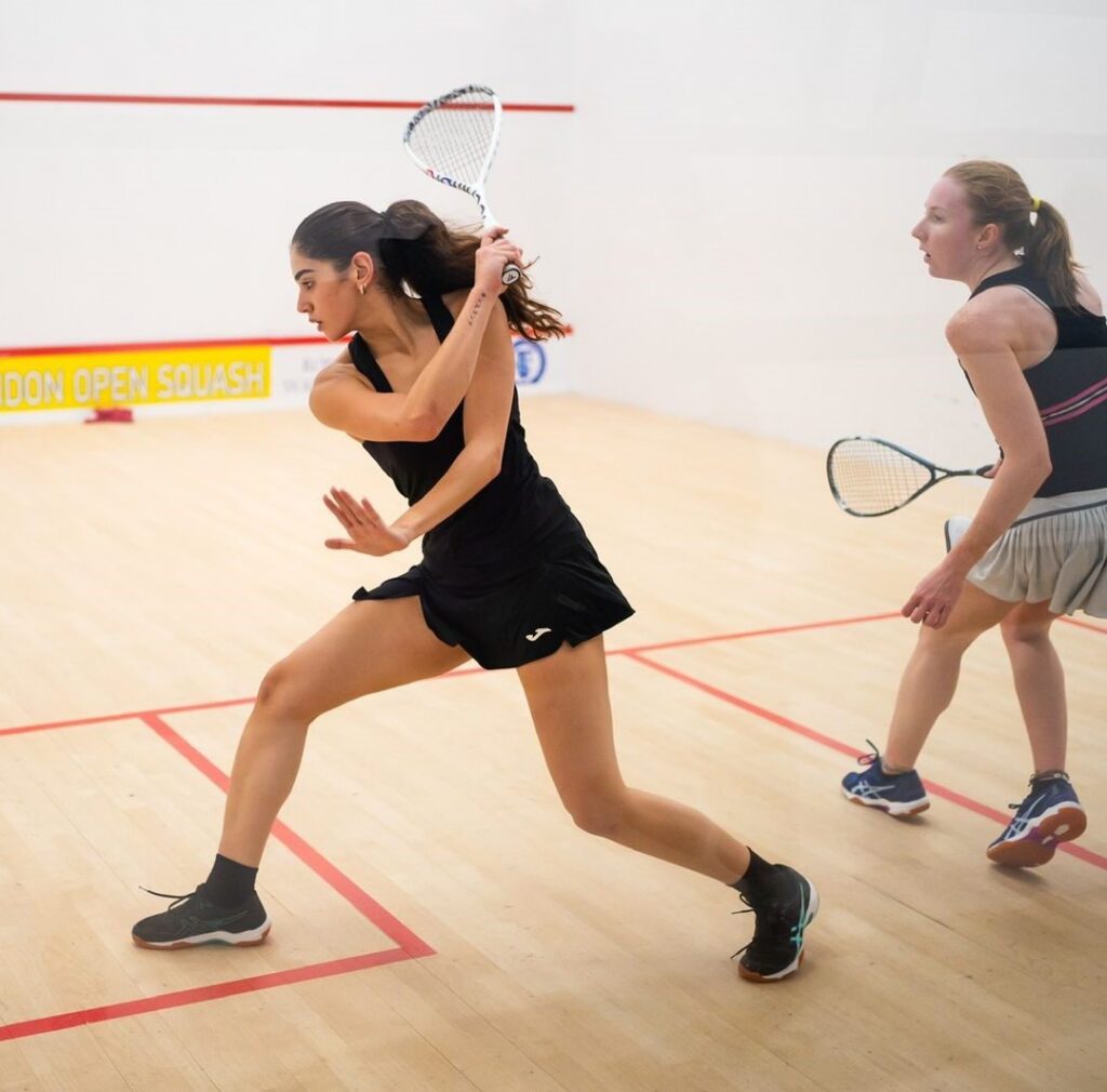 Hana Ismail playing squash in one of our squash courts, swinging to hit the ball.